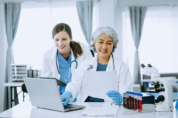 Medical team having a meeting with doctors in white lab coats and surgical scrubs seated at a table discussing a patients working online using computers in the medical industry..