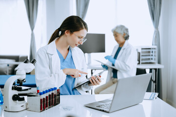Fototapeta premium Two scientist or medical technician working, having a medical discuss meeting with an Asian senior female scientist supervisor in the laboratory with online reading, test samples and innovation