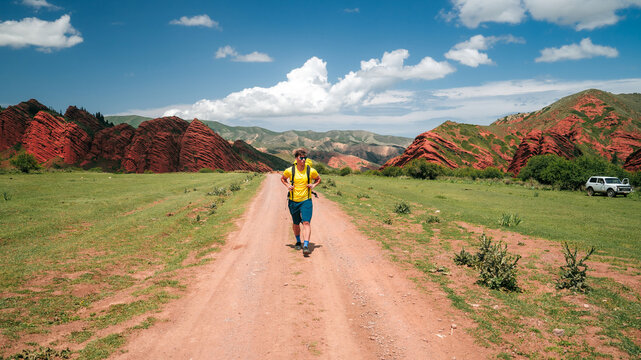 Traveler man in walking on gravel road at breathtaking beauty of Jety Oguz gorge of Kyrgyzstan. Male hiker enjoying view of hill peaks. Concept of sport