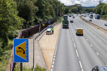 Car rescue worker stands close to traffic in refuge on smart motorway - obrazy, fototapety, plakaty