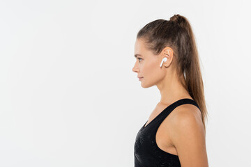 Side view of sportswoman in black sportswear using wireless earphone isolated on white