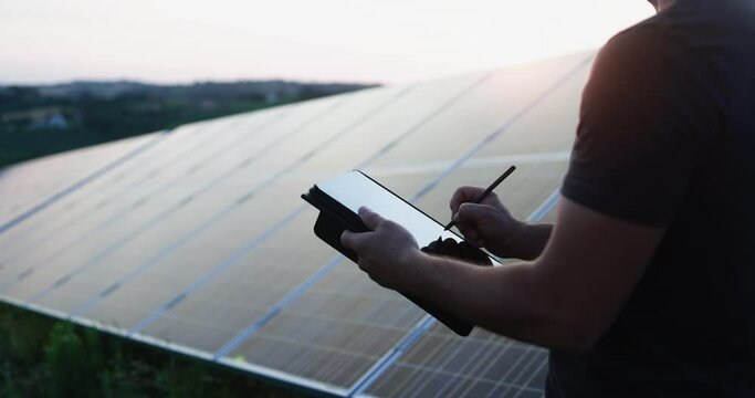 Engineer man working at solar power station outdoor while using digital tablet - Renewable green energy and environmental concept