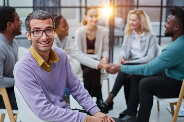 Fototapeta na wymiar A happy young businessman, in a purple sweater, sits against the background of his colleagues