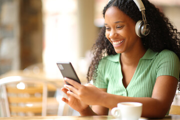 Happy black woman listening audiobook in a restaurant