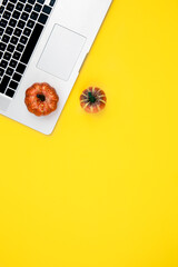 Laptop and pumpkins on a yellow background, top view.