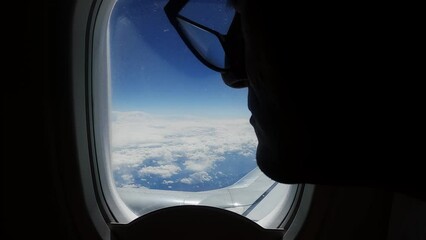 Nostalgic sad man look on plane wing through window on flight over clouds against blue sky - Powered by Adobe