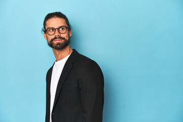 Businessman in suit with eyeglasses and beard looks aside smiling, cheerful and pleasant.