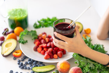 A glass of smoothie from berries in a child's hand at home in the kitchen.