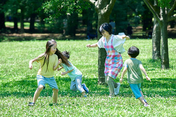 追いかけっこをして遊ぶ子供たちとエプロン姿の女性