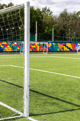 Artificial turf on the football field. Part of the football goal and green synthetic grass on the sports field on the background of colorful seats.