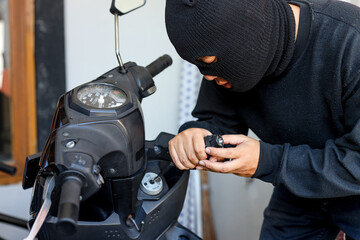 Motorcycle thief in black mask trying to unlock the ignition key of motorcycle with screwdriver....