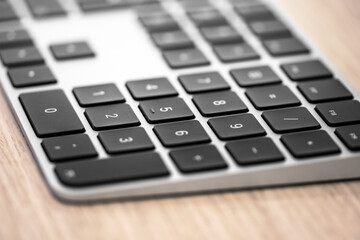 Wireless aluminum keyboard, on wooden desk, focus on button.