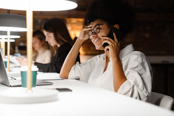 Young african woman talking on cellphone while working in office