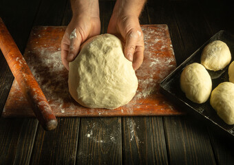 Close-up of baker hands knead dough with flour for baking pies. Working environment on the kitchen table in the bakery