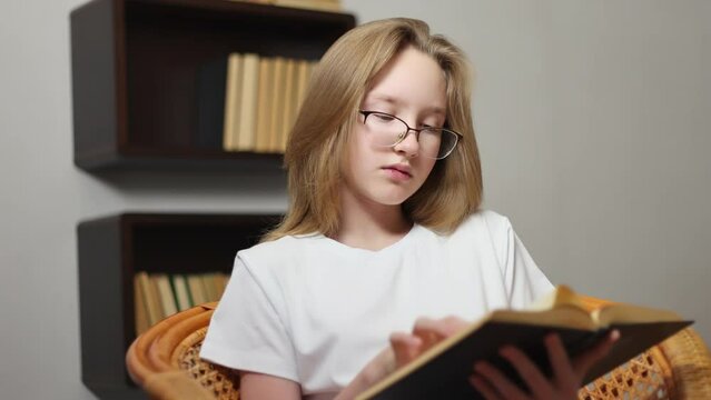 A teenage girl is reading a book on a bamboo chair.
