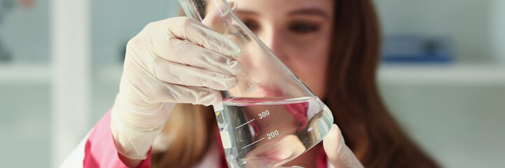 A young woman laboratory assistant looks at flask water