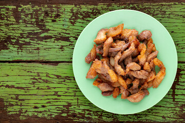 tasty fried pork in green ceramic plate on rustic old green natural wood texture background with copy space for text, top view, flat lay, street food
