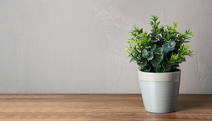 Beautiful artificial plant in flower pot on wooden table near grey wall, space for text