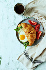 Croissant with fried egg, arugula and black coffee on kitchen table. Top view. Copy space