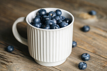 Fresh raw organic farm blueberry in white cup on rustic wooden background, close up.
