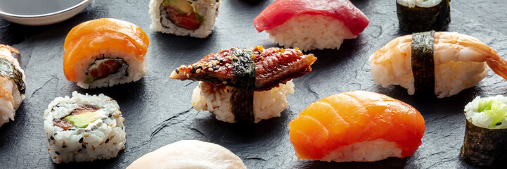 Sushi panorama. Nigiri with eel, salmon, shrimp on a black background, Japanese food on a plate at an Asian restaurant
