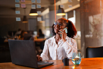 Black businesswoman working on laptop. Portrait of beautiful businesswoman in the office. Woman taking to the phone.