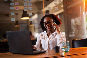 Black businesswoman working on laptop. Portrait of beautiful businesswoman in the office. Woman taking to the phone.