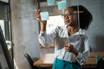 Businesswoman in conference room. Young African businesswoman making a business plan. Woman writing on the glass board in office.