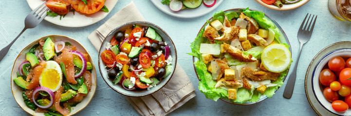 Fresh salads panorama, overhead flat lay shot of an assortment. Variety of plates and bowls with green vegetables. Healthy food, top shot, panoramic banner