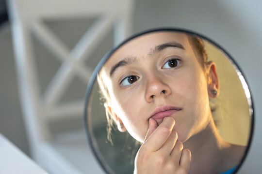 A teenage girl looks thoughtfully at her reflection in the mirror.