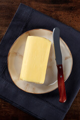A stick of fresh butter, top shot on a dark rustic wooden table, with a knife