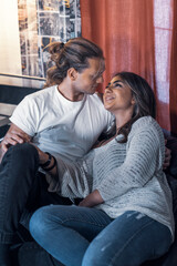 Obraz premium Inside house couple shooting sitting on sofa relaxing and looking at each other eyes smiling - Yellow and blue atmosphere tone light. Lovers shot talking in house studio red courtain