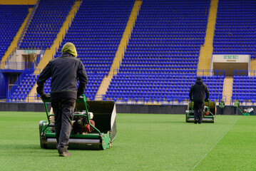 Workers at the stadium cutting grass on football stadium.