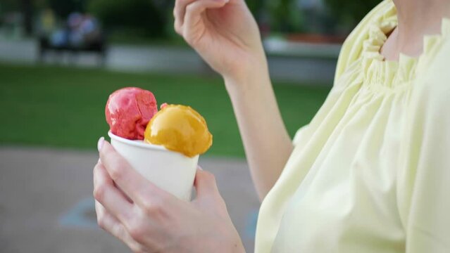 Woman eating ice cream while walking in city, closeup. Camera moving left