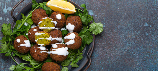 Plate of fried falafel balls served with fresh green cilantro and lemon top view on rustic concrete background. Traditional vegan dish of Middle Eastern cuisine, space for text