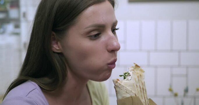 Beautiful young woman eating tasty fresh shawarma in cafe