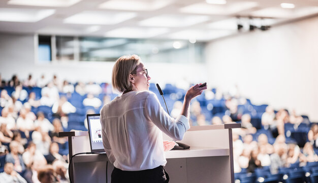Female speaker giving a talk on corporate business conference. Unrecognizable people in audience at conference hall. Business and Entrepreneurship event
