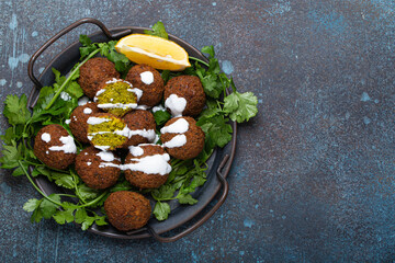 Plate of fried falafel balls served with fresh green cilantro and lemon top view on rustic concrete background. Traditional vegan dish of Middle Eastern cuisine, space for text - obrazy, fototapety, plakaty