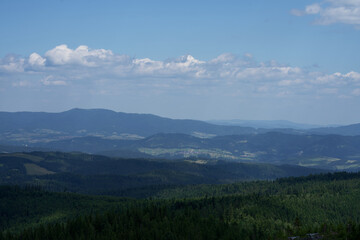 Obraz premium zdjęcie przedstawiające krajobraz górski wysokie szczyty i doliny nad którymi jest niebieskie niebo z kłębiącymi się chmurami. Lasy w dolinach gór, krajobraz górski natura i cisza i spokój