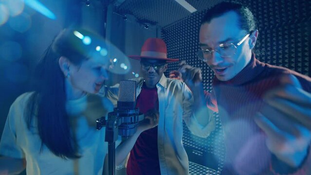 A group of performers are singing into a mic in the music studio