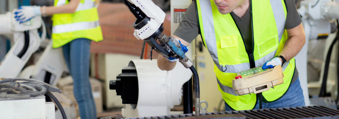 Young caucasian engineer man using remote control with ai robot machine arm automatic for manufacture production at the factory, robotic electronic and intelligence technology, industry concept.