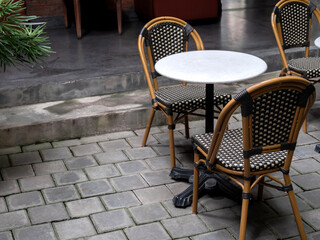 Empty comfortable vintage rattan chair seats with round marble table decorated on grey concrete brick tile floor inside the natural dim light building with copy space. Cozy living zone interior.