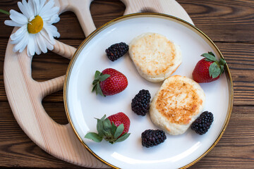 Morning breakfast with cheesecakes and strawberries and blackberries. Cooked breakfast is dietary and healthy
