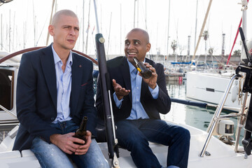 Latin American and European businessmen sit and drink beer on the yacht in seaport