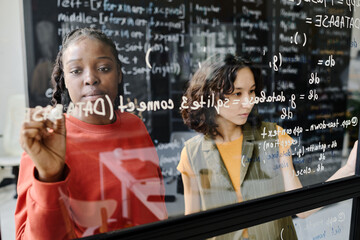 Teacher writing codes on blackboard together with student in the classroom