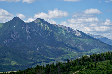 Góry piękne zdjęcie przedstawiające krajobraz górski wysokie szczyty i doliny nad którymi jest niebieskie niebo z kłębiącymi się chmurami.  - obrazy, fototapety, plakaty