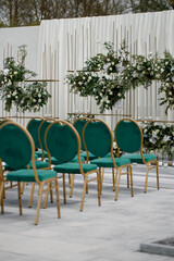 Wedding decor, emerald-colored chairs, against a background of flowers. Side view.