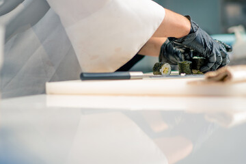 A sushi chef prepares maki rolls using nori avocado rice and a bamboo mat to make sushi in the kitchen of a sushi restaurant 