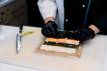 Sushi chef in the process of preparing a Philadelphia roll with salmon cream cheese shrimp and chuka seaweed on a bamboo sushi mat