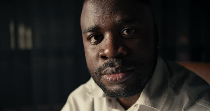 Close-up portrait of a Black-skinned man in a white shirt who looks at the camera and does not smile